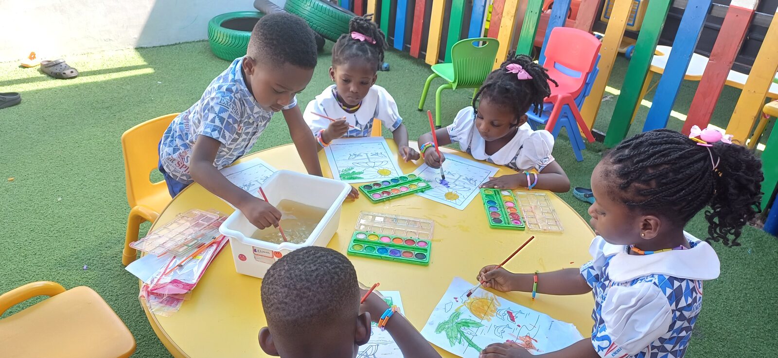Children painting with watercolours together at an outdoor table